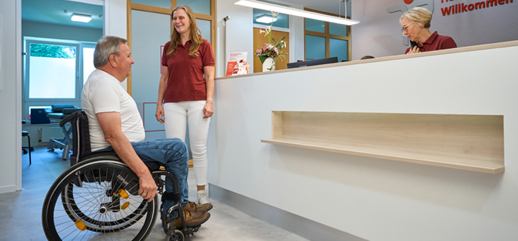 Patient im Rollstuhl in Physiopraxis in Paderborn wird freundlich von Therapeutin begrüßt.