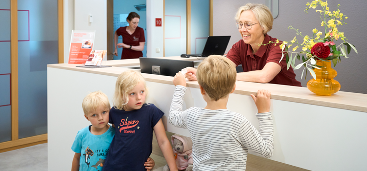 Kinder an der Anmeldung in der Physiotherapiepraxis in Paderborn im Austausch mit der Kollegin von der Verwaltung.
