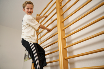 Junge klettert im Rahmen der Krankengymnastik an einer Sprossenwand zur Rumpfstabilisation.