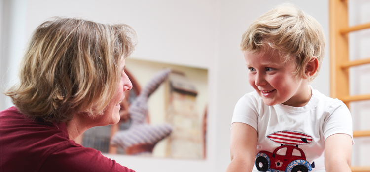 Therapeutin spricht mit Kind während einer Kinderbehandlung nach dem Bobath-Konzept.